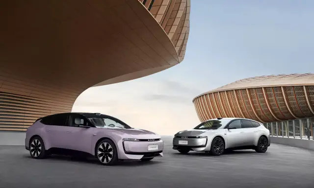 Deux Audi E5 Sportback, une lilas et une argentée, se présentent devant des bâtiments aux formes organiques.