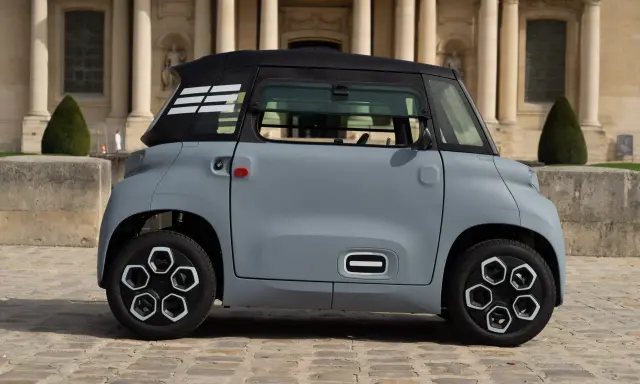 Une petite voiture grise, un ami pour la ville, se gare devant un bâtiment imposant.