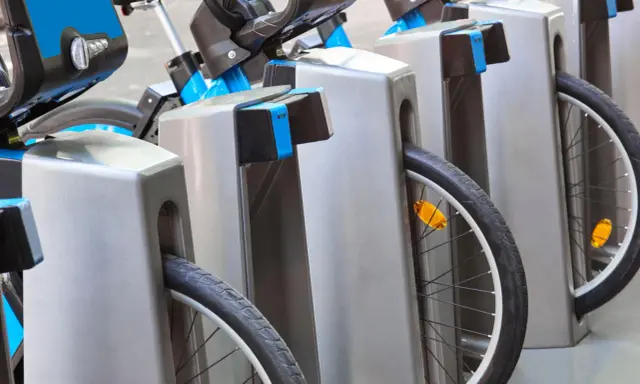 Des vélos bleus et gris sont rangés, prêts à recharger sur une borne auto.