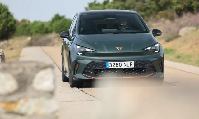 La Cupra Born VZ, d'un vert profond, roule sur une route de campagne. Un conducteur porte des lunettes de soleil.