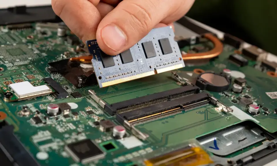 Main d'une personne installant un module de test RAM sur une carte mère d'ordinateur portable.