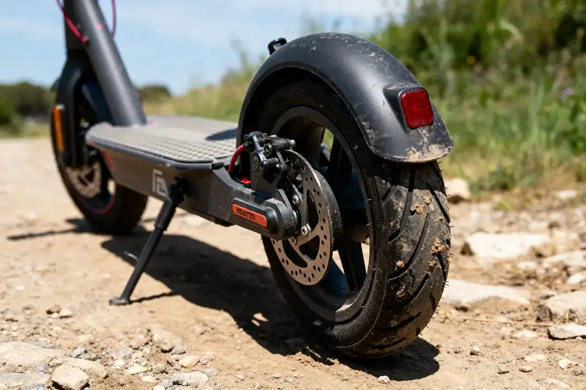 Roues de trottinette électrique sur terrain rocailleux. Le pneu arrière est sale, suggérant qu'il est impossible de gonfler le pneu de la trottinette.