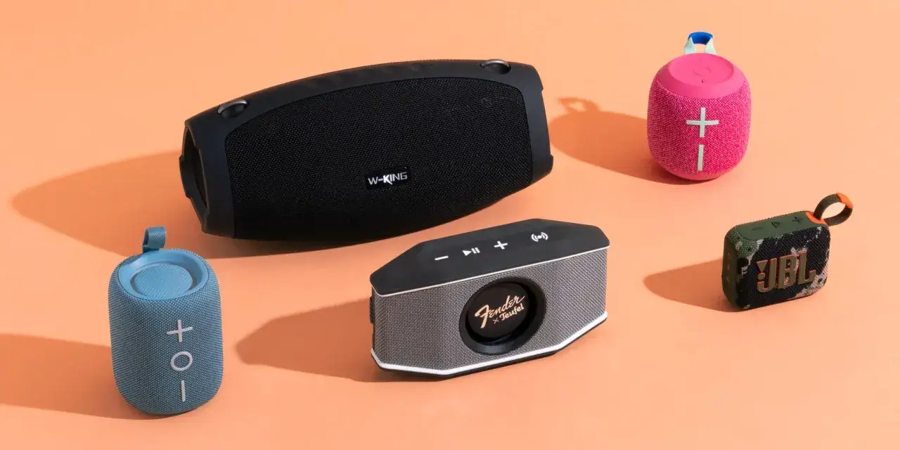 Plusieurs enceintes Bluetooth de différentes tailles et couleurs sont disposées sur un fond orange. Idéal pour savoir comment choisir une enceinte Bluetooth.