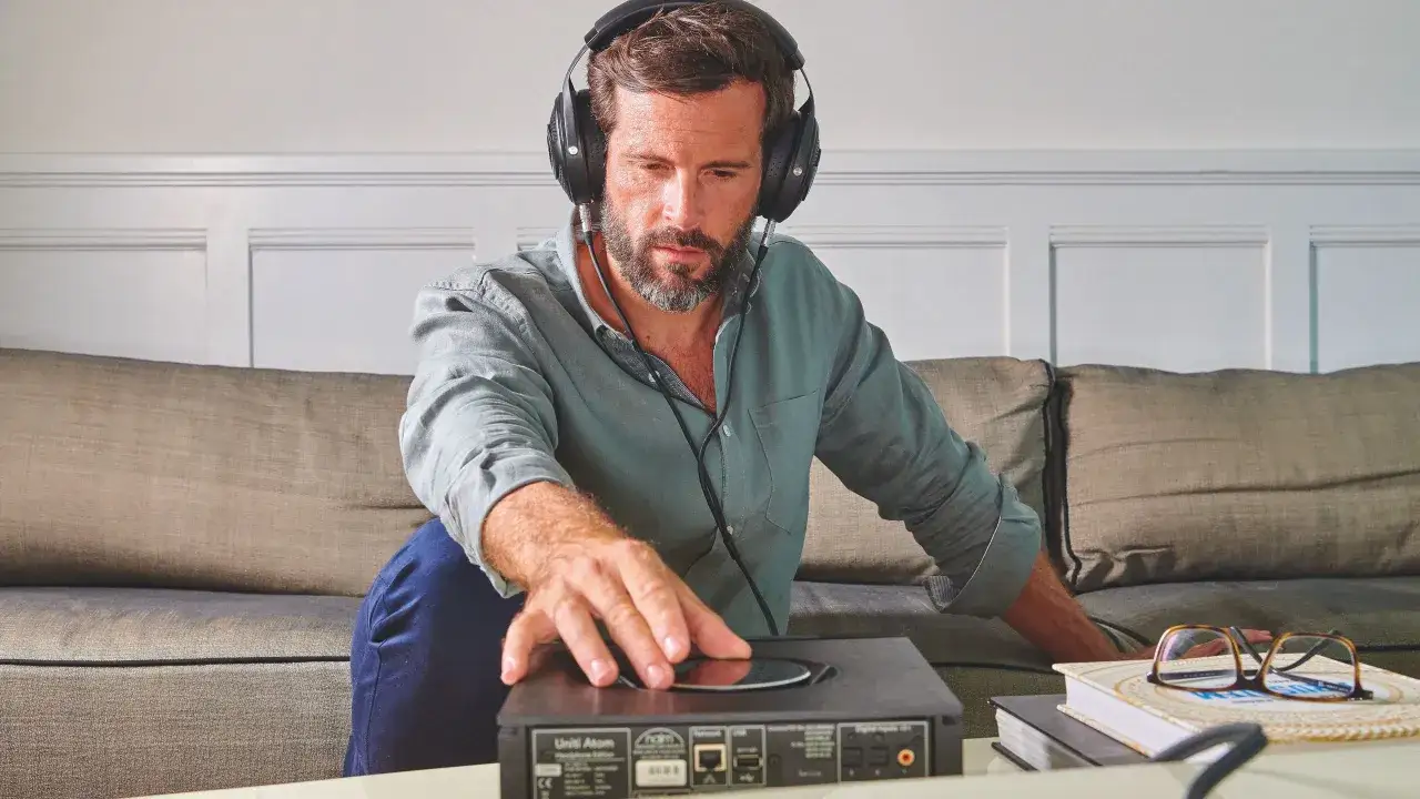 Homme avec casque audio, ajustant un appareil. La sensibilité du casque audio est mise en avant par son écoute attentive.