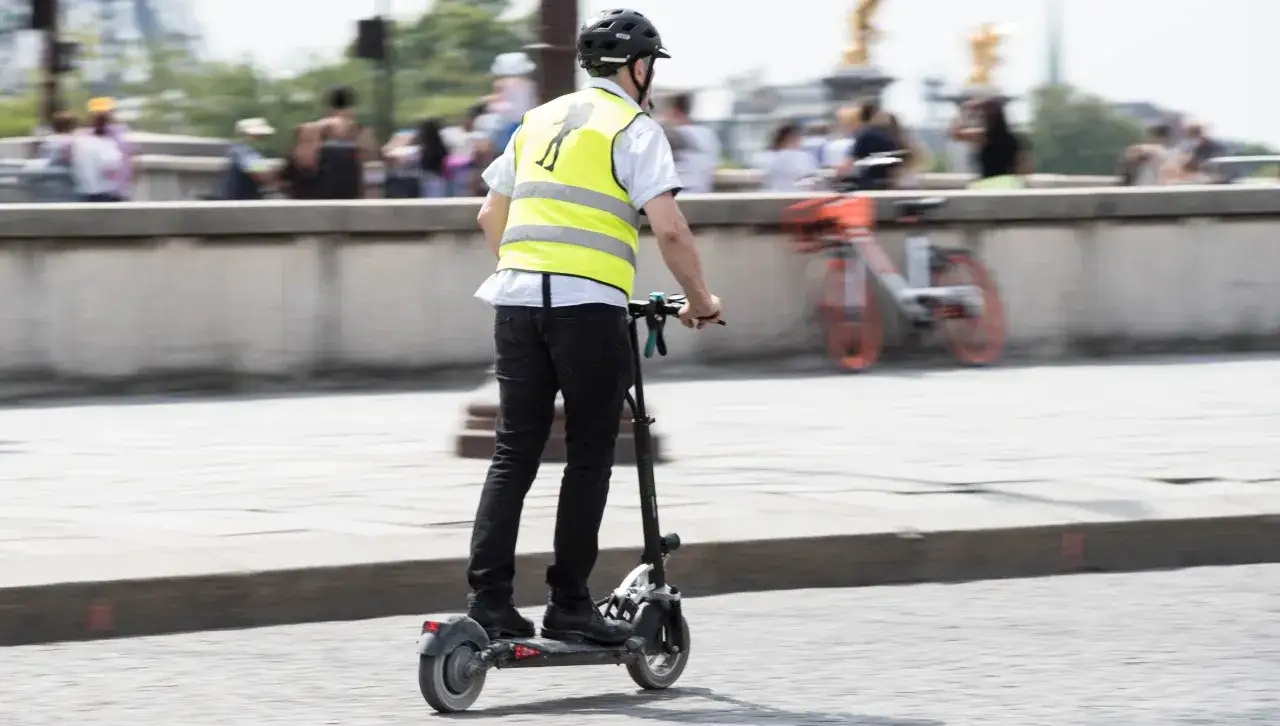 Un homme en trottinette électrique, portant un gilet jaune, roule sur la route. La question 