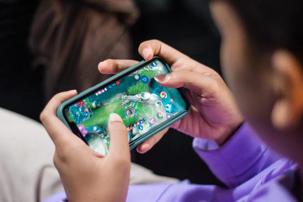 Un jeune joueur concentré sur son smartphone, naviguant dans un univers de jeu. Il est en train de découvrir l'un des meilleurs jeux mobile gratuit.