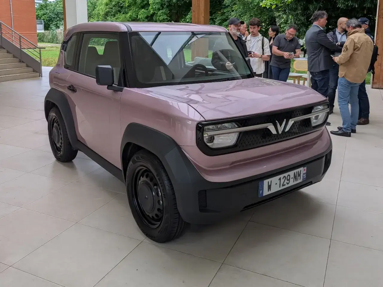 Le VinFast VF3 rose pâle, un petit SUV urbain, est présenté à un groupe de personnes.