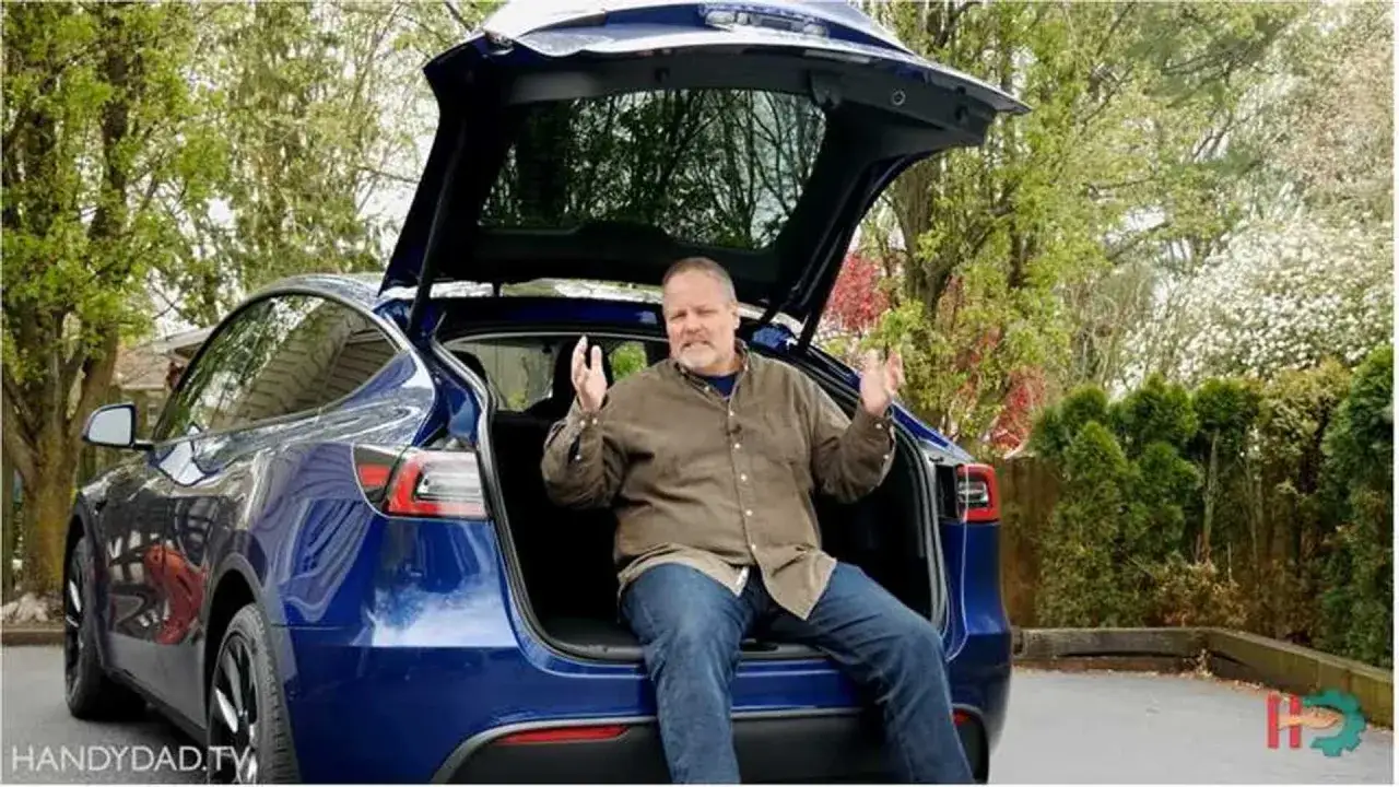 Un homme est assis dans le coffre ouvert d'une Tesla Model Y bleue, expliquant ses fonctionnalités.