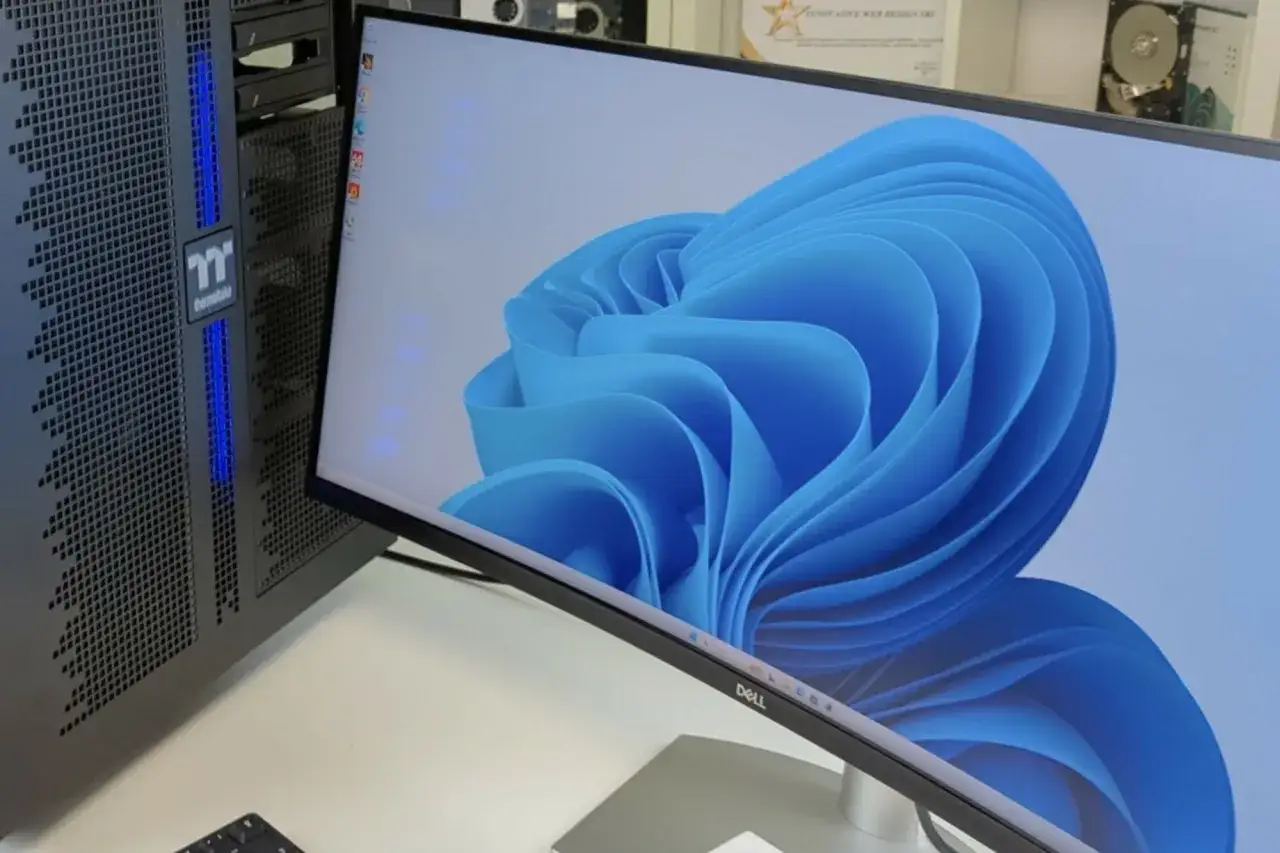 Un ordinateur avec une tour Thermaltake et un écran Dell, dont la dimension ecran 27 pouces affiche le fond d'écran Windows 11.