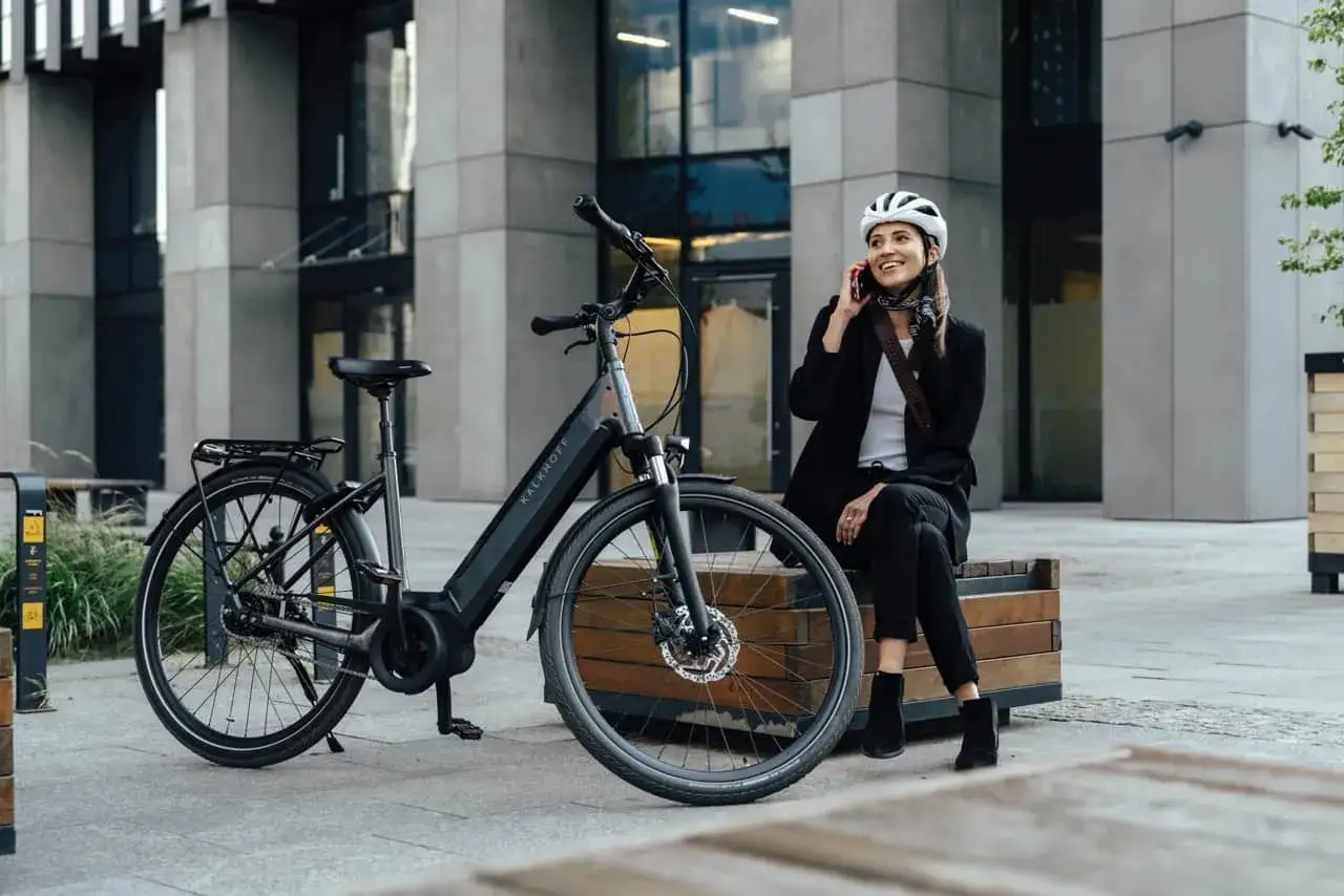Une femme en tenue de ville, casque sur la tête, discute au téléphone à côté de son vélo électrique. Facile à utiliser, il est idéal pour se déplacer en ville.
