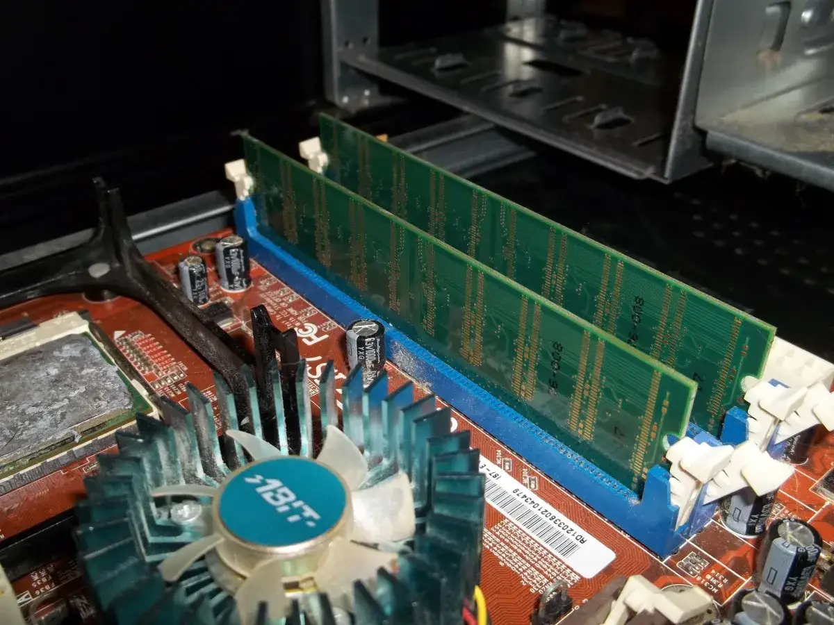 Deux barrettes de RAM verte sur une carte mère rouge. Un ventilateur bleu est visible. Un probleme ram pc peut venir de là.