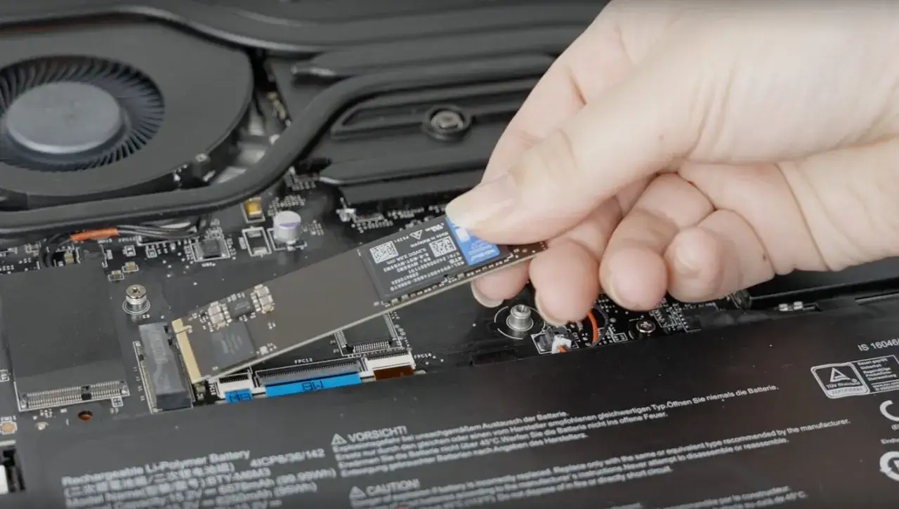 Main d'une personne tenant un SSD pour l'installer dans un ordinateur portable.