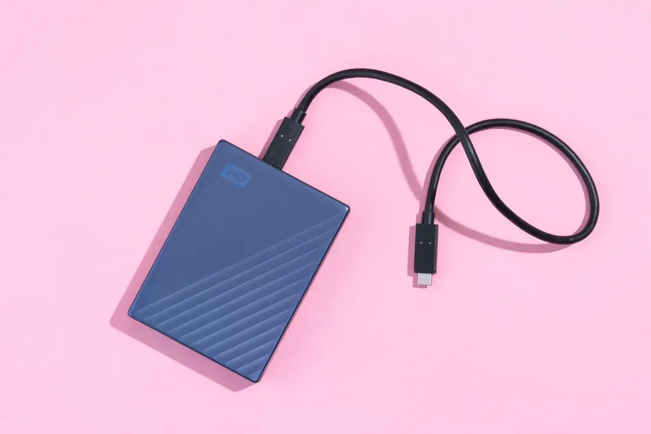 Disque dur externe bleu WD avec câble USB-C sur fond rose. Guide pour comment choisir un disque dur externe.