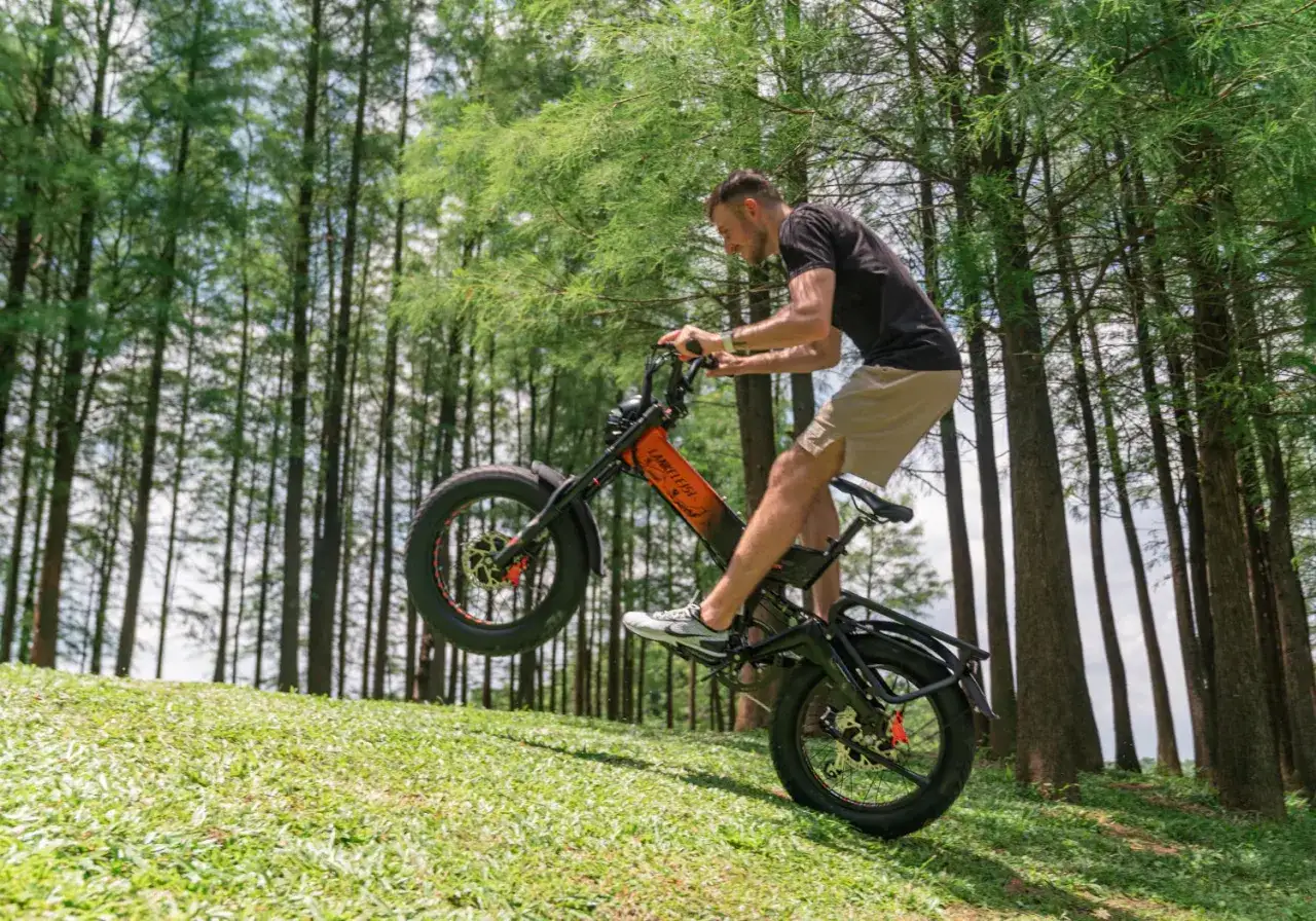 Un homme fait du vélo électrique sur une pente herbeuse, le pneu avant en l'air. Il semble s'amuser, explorant quelle vitesse pour monter une côte en vélo électrique.