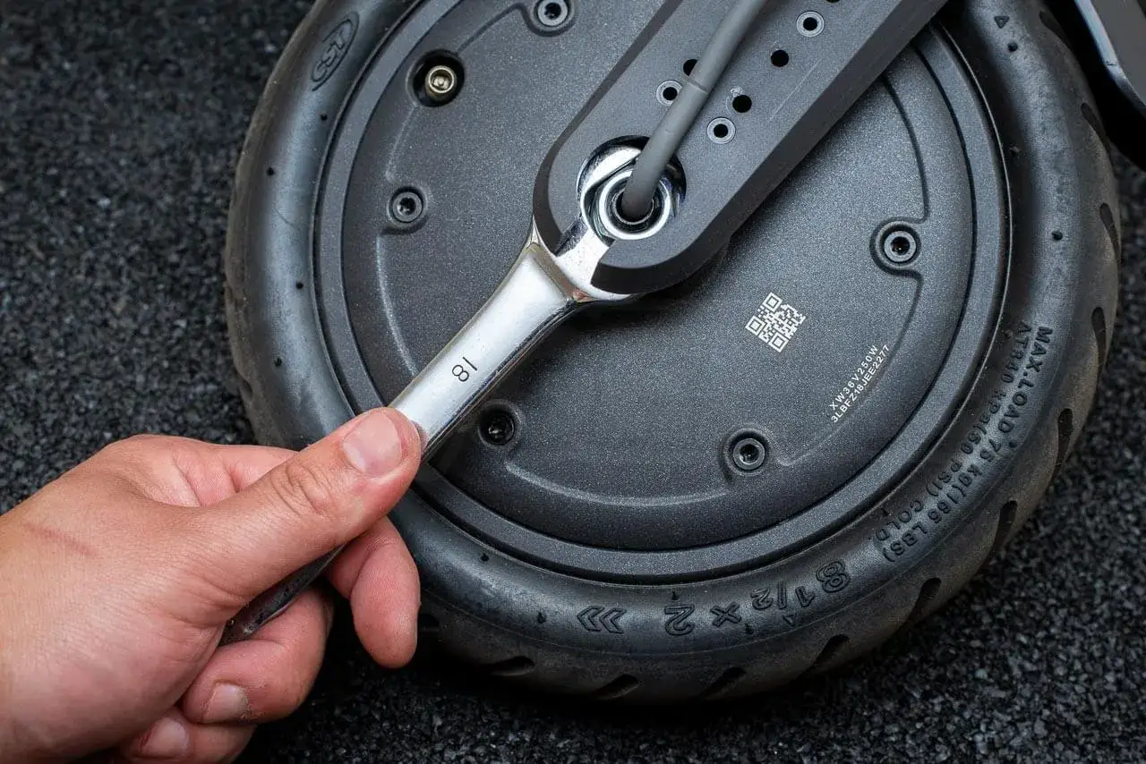 Main d'une personne utilisant une clé pour changer la roue avant d'une trottinette électrique.