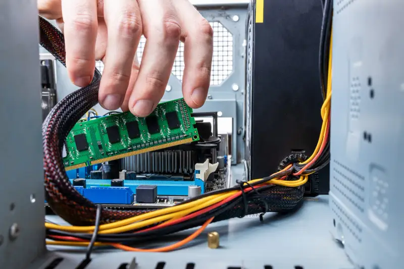 Main d'un homme insérant une barrette de RAM verte dans un emplacement de carte mère. Guide pour comment installer RAM.